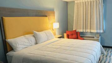 A hotel room with a large bed, a nightstand, a lamp, and a window with blinds.
