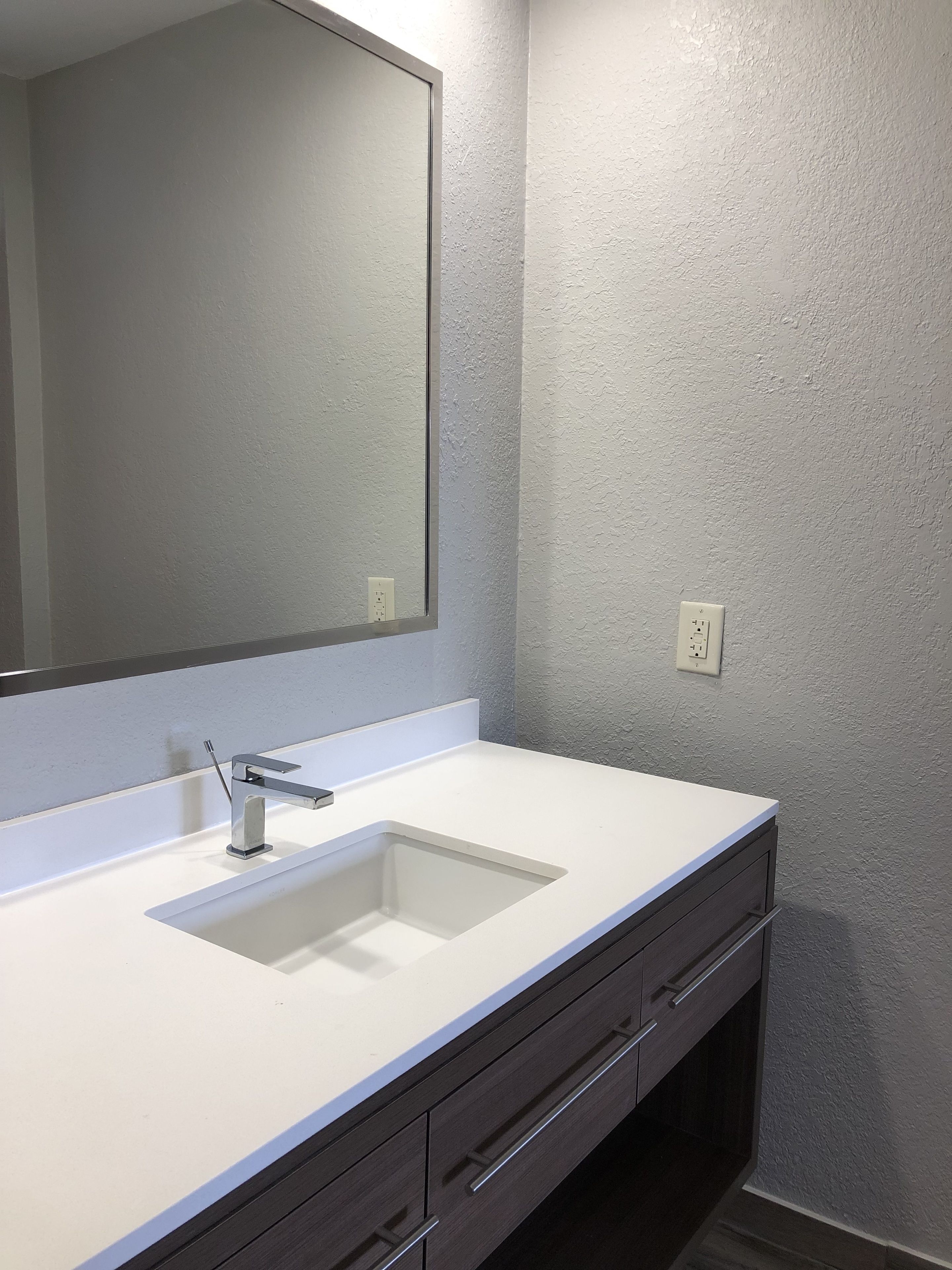 Un baño con un lavabo blanco, un espejo y un mueble de tocador de madera oscura.