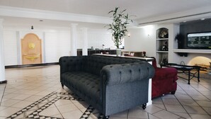 A spacious living area with a dark grey sofa, a red velvet chair, and a large flat-screen TV mounted on the wall. - All Seasons Inn & Suites (Memphis)