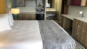 A hotel room with a bed, a desk, a microwave, a refrigerator, a sink, and a mirror. - All Seasons Inn & Suites (Memphis)