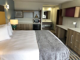 Una habitación de hotel con cama, escritorio, microondas, refrigerador, lavamanos y espejo.