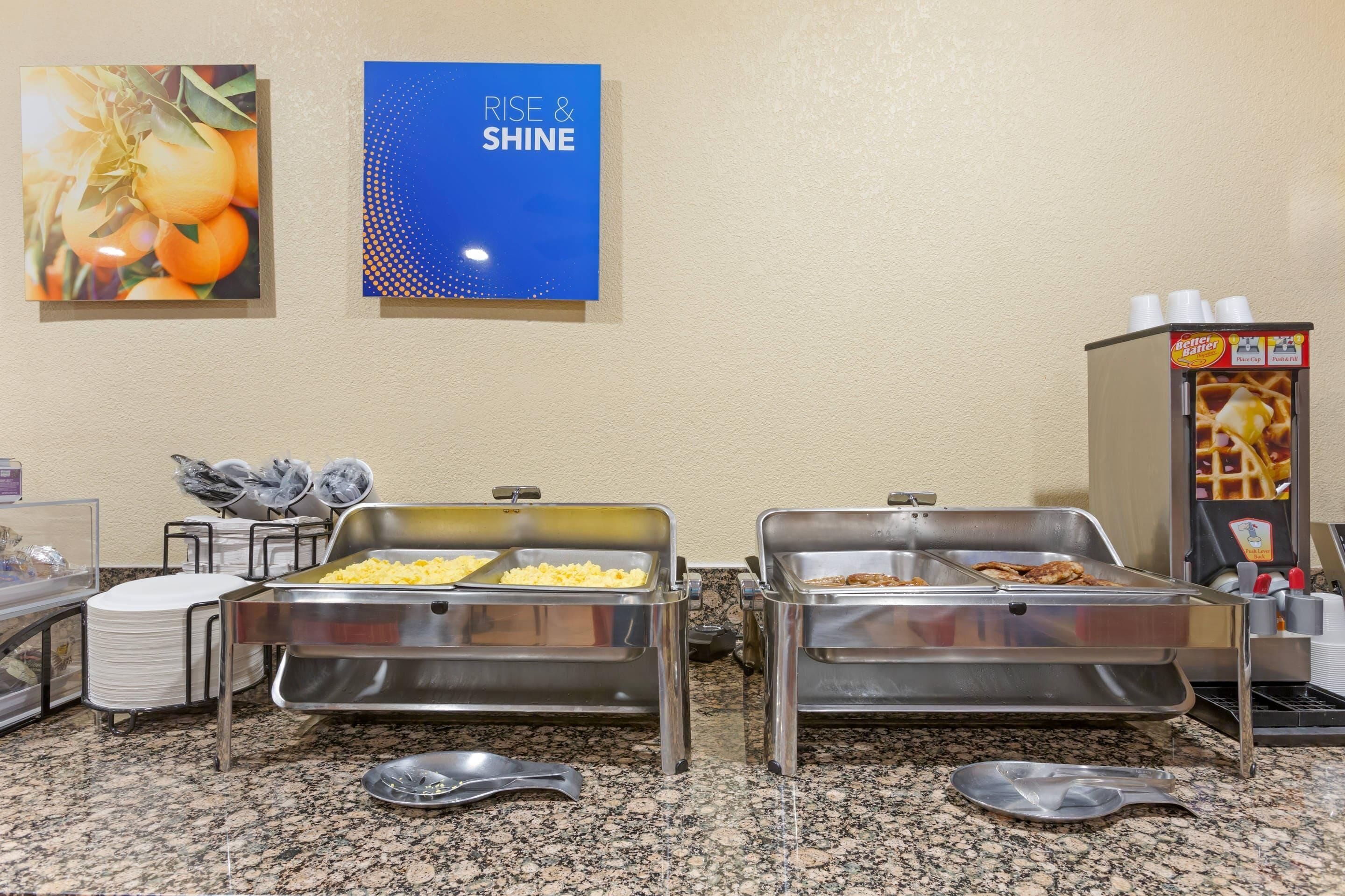 Montaje de buffet con dos bandejas de servicio abiertas, una máquina para gofres y un dispensador de bebidas.
