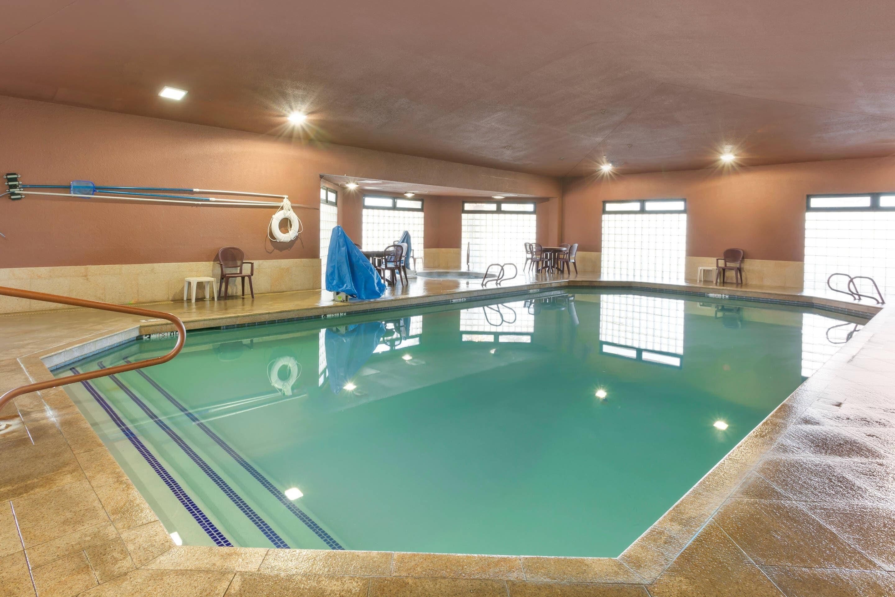 Una piscina interior con agua cristalina, un trampolín y una zona de estar con sillas y mesas.