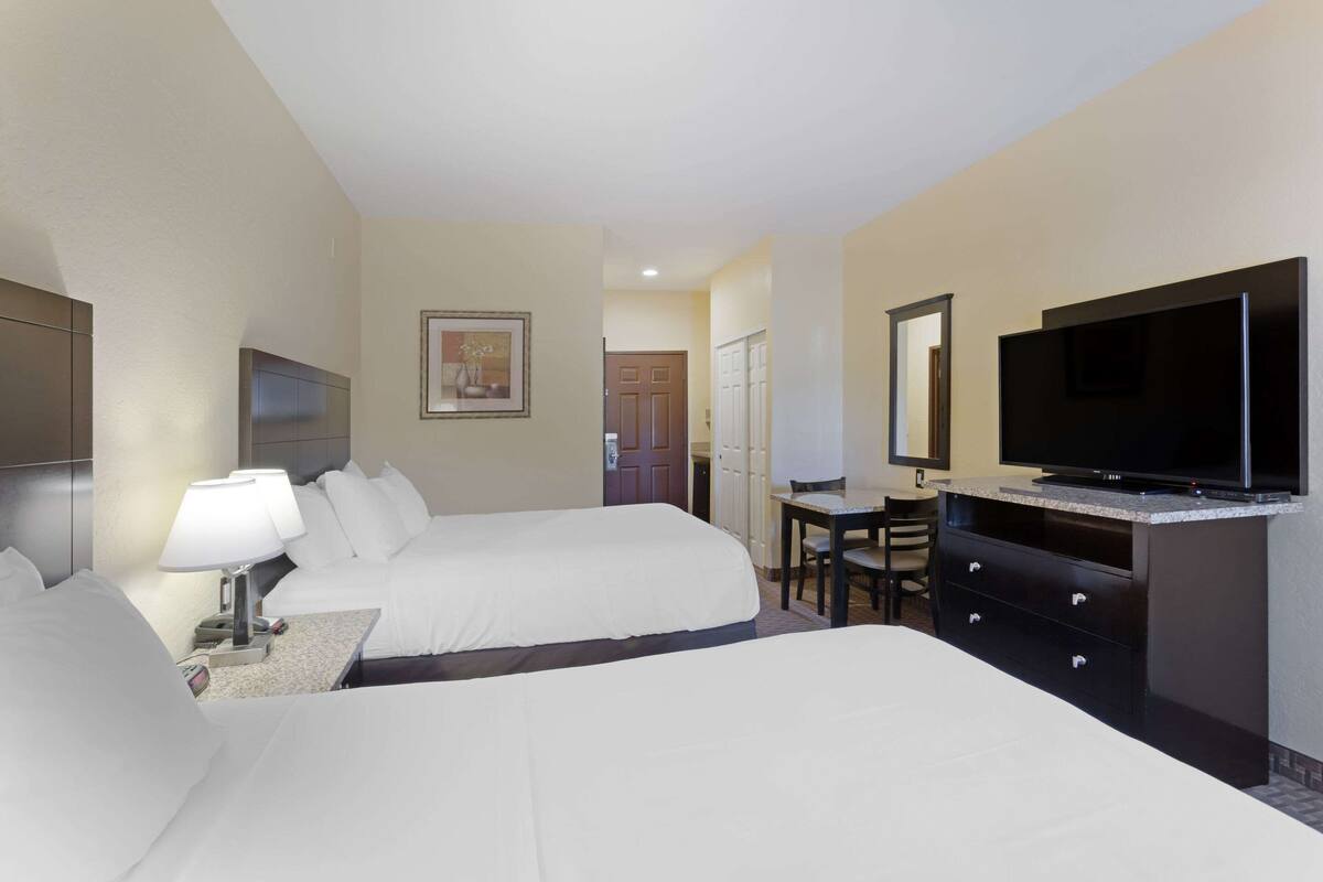 A hotel room with two beds, a desk, a television, and a mirror.