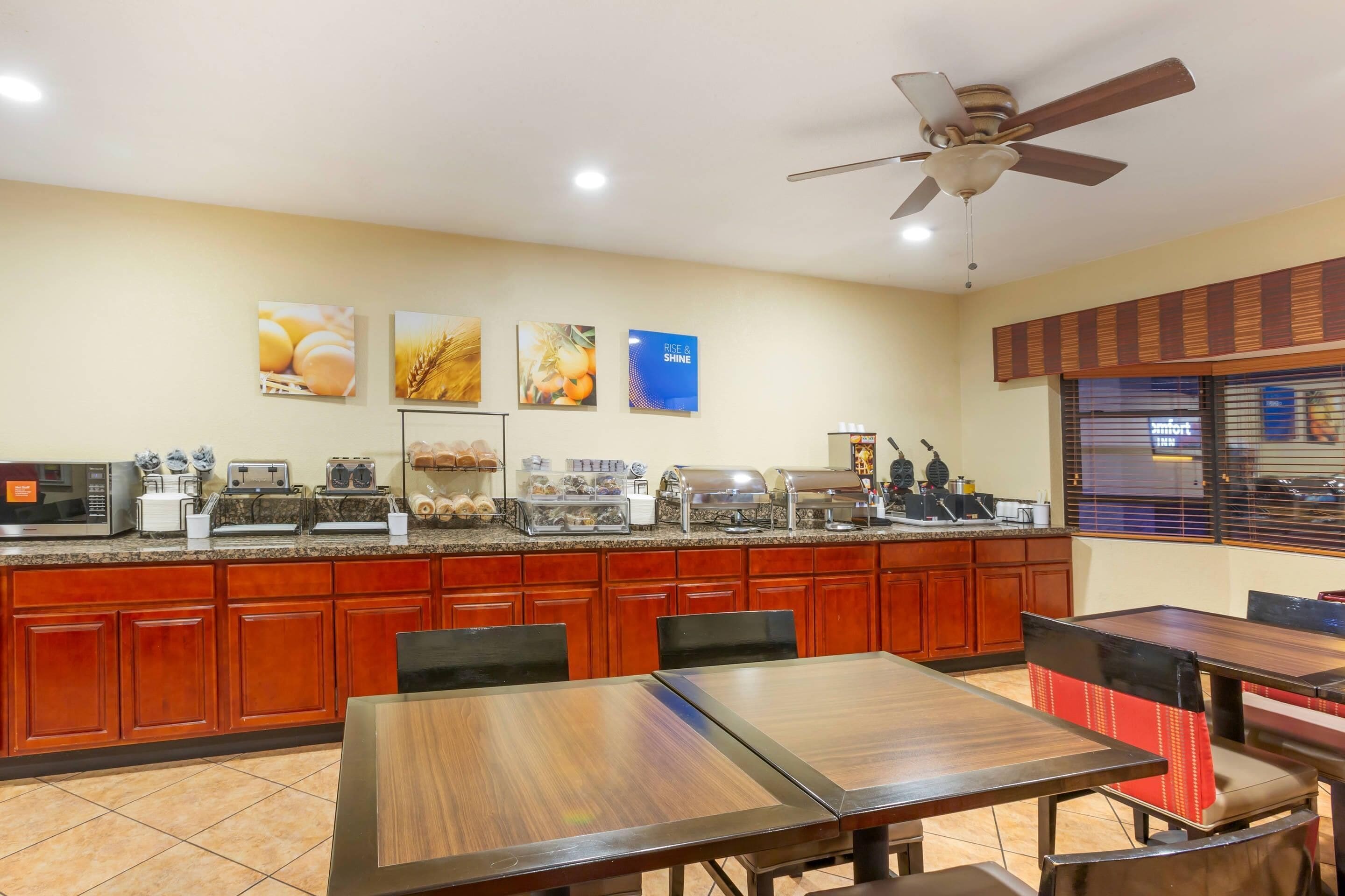 A hotel dining area with a buffet setup, wooden cabinets, and a ceiling fan.