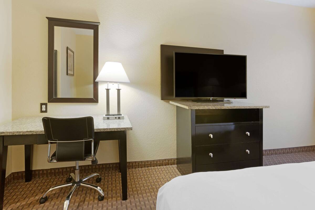 A hotel room with a bed, a desk with a chair, a television, and a dresser.