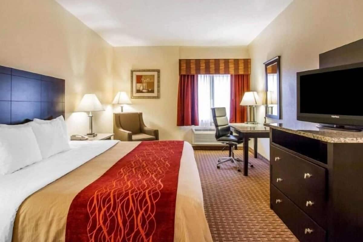 A hotel room with a bed, desk, chair, TV, and a painting on the wall.