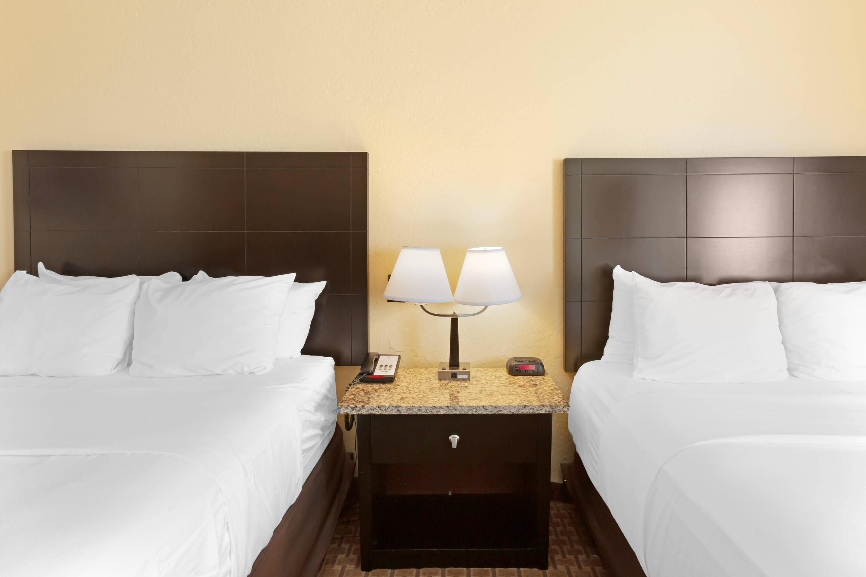 A hotel room with two beds, a nightstand with a lamp, a phone, and a digital clock.