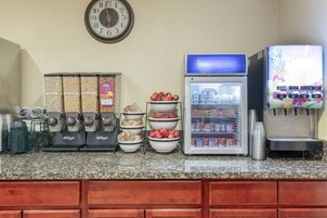 Una estación de bebidas de autoservicio con refrigerador, dispensador de jugo y máquina de café.