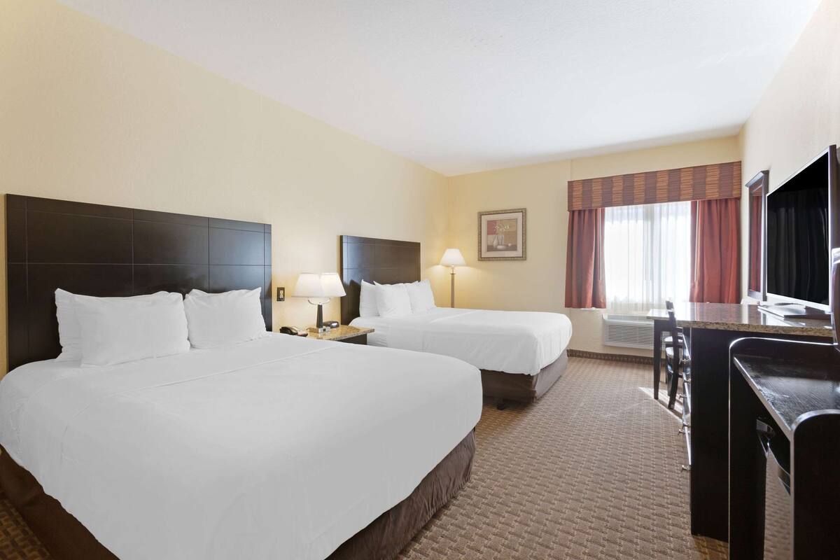 A hotel room with two beds, a desk, a television, and a window with curtains.