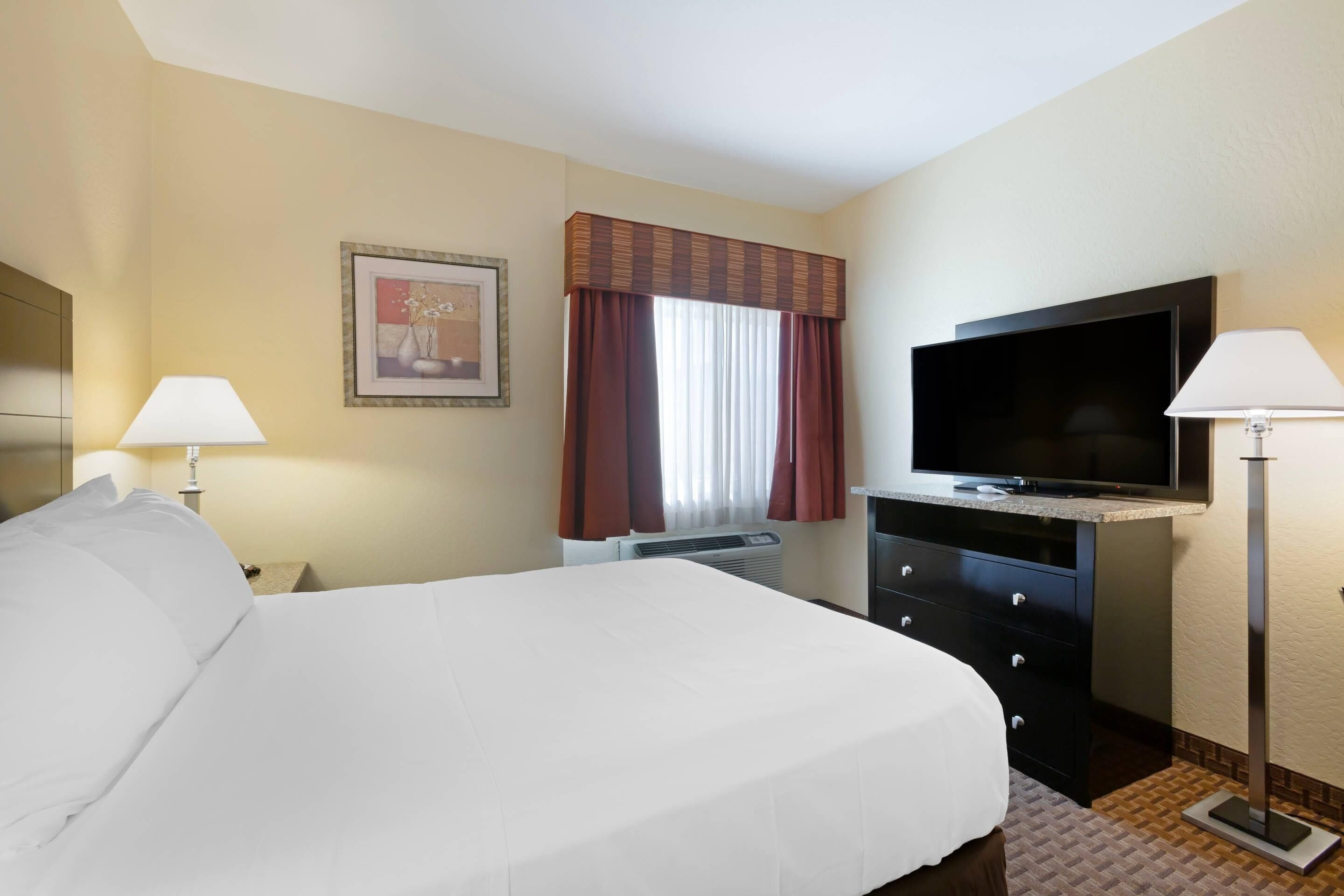 A hotel room with a bed, a television, a desk, and a window with curtains.