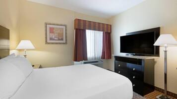 A hotel room with a bed, a television, a desk, and a window with curtains.