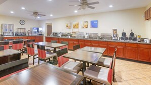 A hotel dining area with multiple tables and chairs, a kitchen in the background, and ceiling fans. - Comfort Inn Near Grand Canyon (Williams)