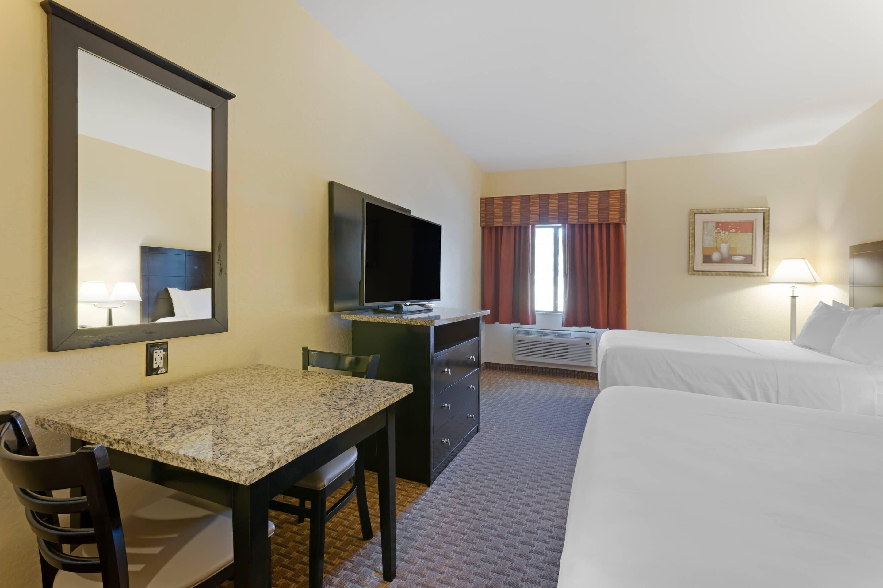 Habitación de hotel con cama, escritorio, silla, televisor y ventana con cortinas.