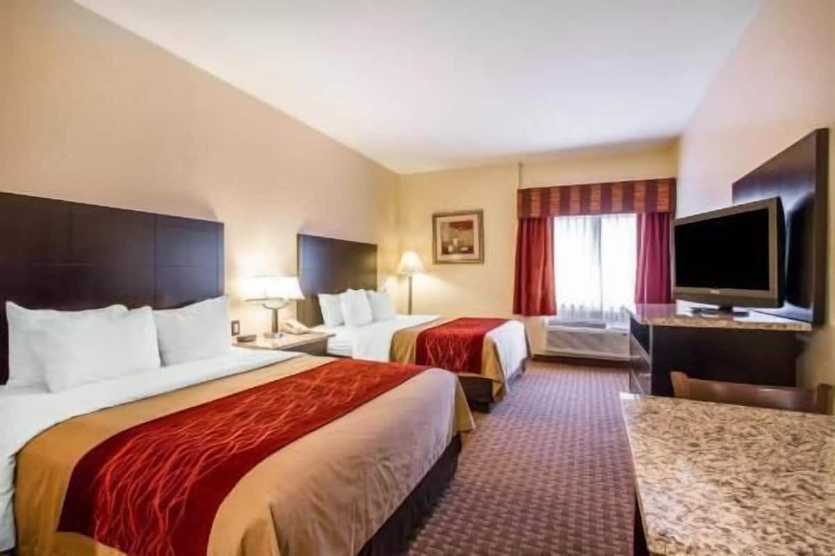 A hotel room with two beds, a desk, a TV, and a window with curtains.