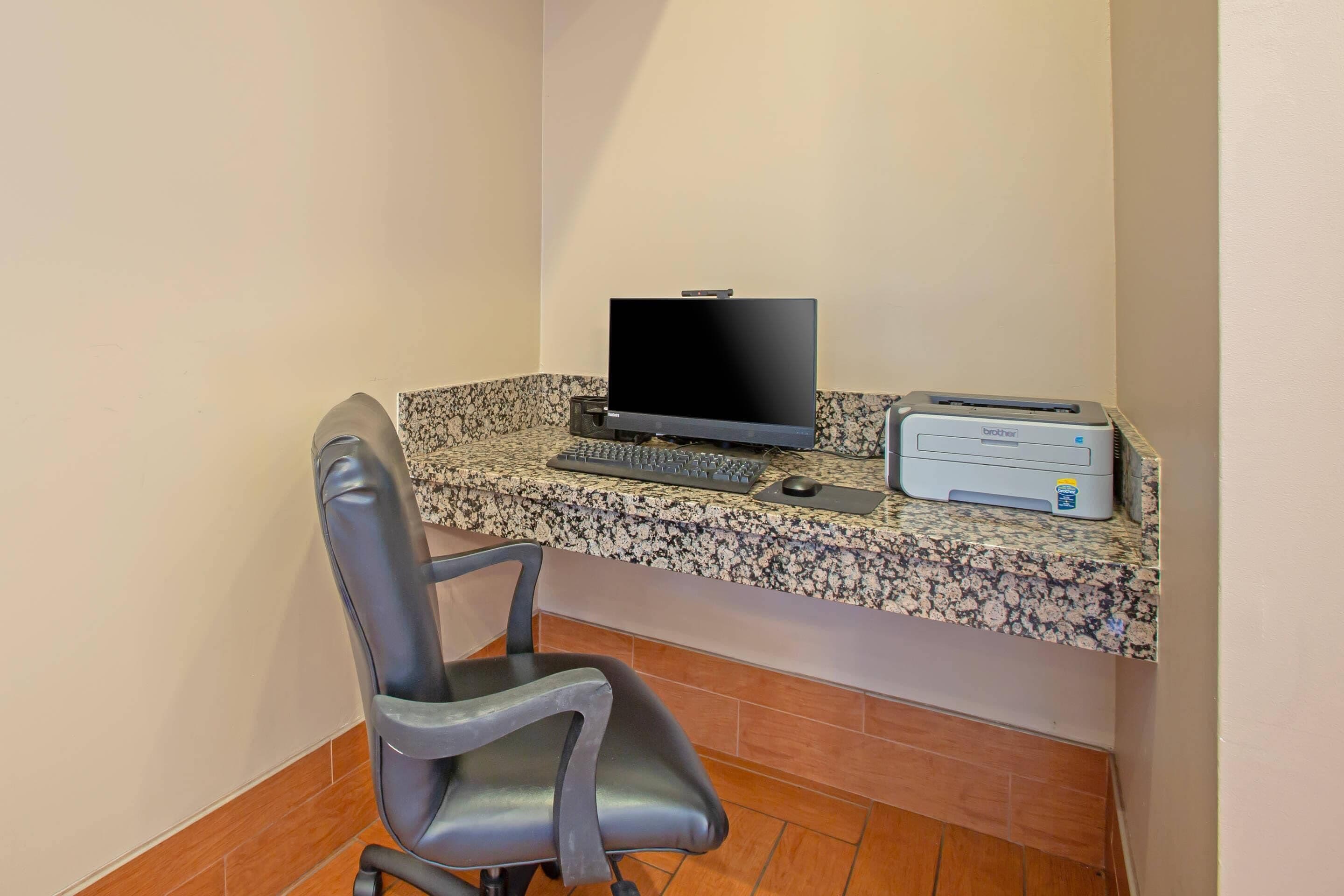 A corner office with a computer, keyboard, mouse, and printer on a granite countertop.
