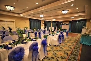 A banquet hall with round tables, chairs with blue sashes, and a stage with curtains.