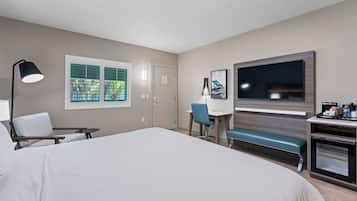 Une chambre d’hôtel avec un grand lit, un bureau avec une chaise, une télévision et une fenêtre avec des stores.