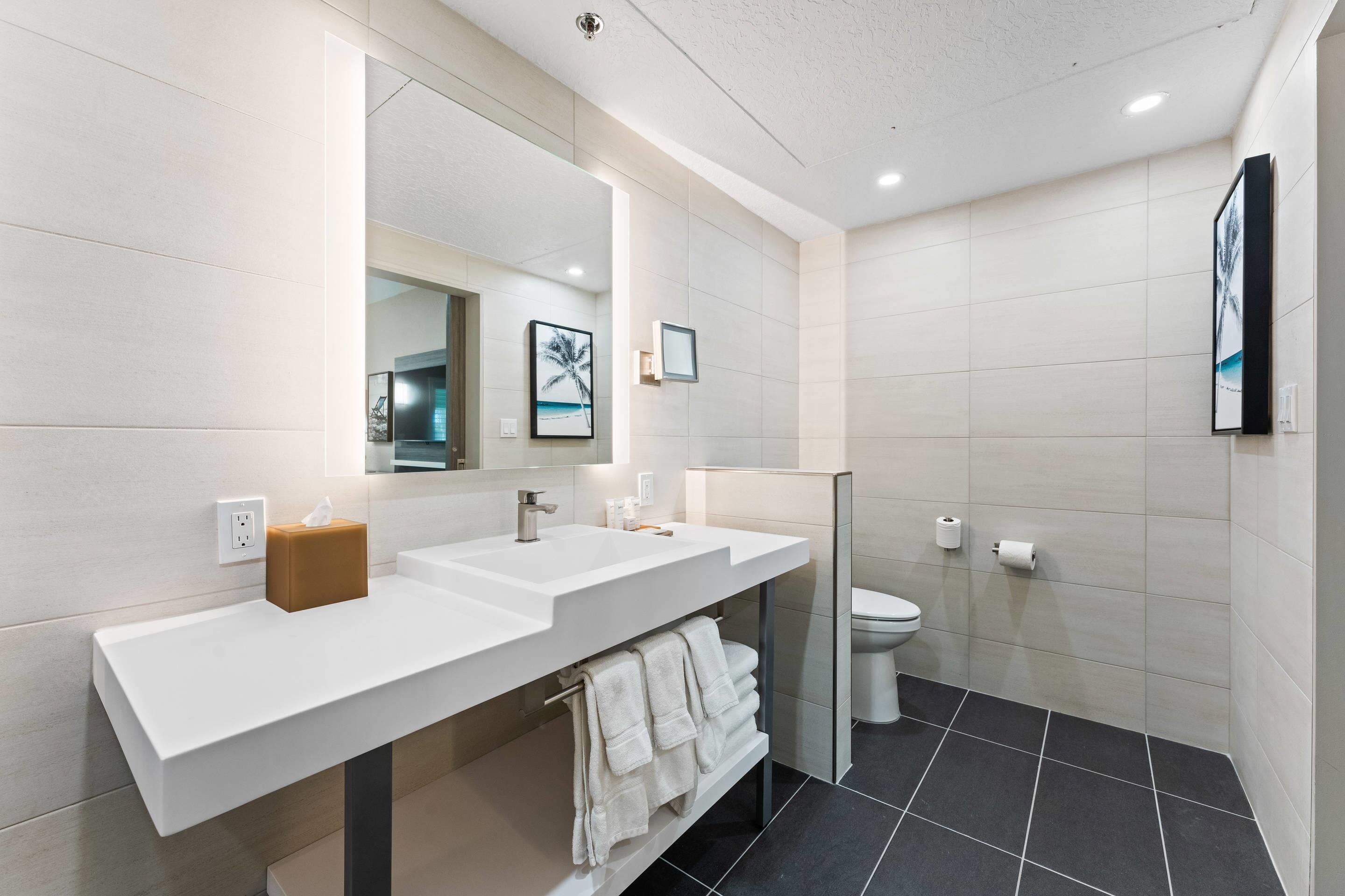 A modern bathroom with a white vanity, a large mirror, a toilet, and a black tiled floor.