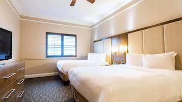 A hotel room with two beds, a TV, a window with blinds, and a ceiling fan.