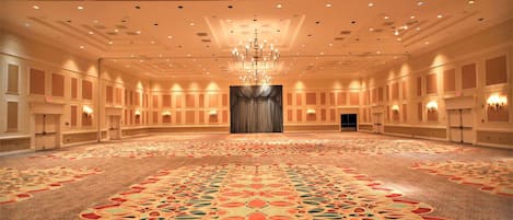 A spacious hotel conference room with a patterned carpet, chandeliers, and a large curtain at the front.