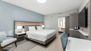 A modern hotel room with a large bed, bedside tables with lamps, a TV, and a seating area with a chair and table. - Radisson Resort at the Port (Cape Canaveral)