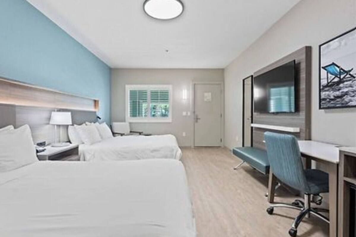 Ein Hotelzimmer mit zwei Betten, einem Schreibtisch, einem Sessel, einem Fernseher und einem Fenster mit Jalousien.