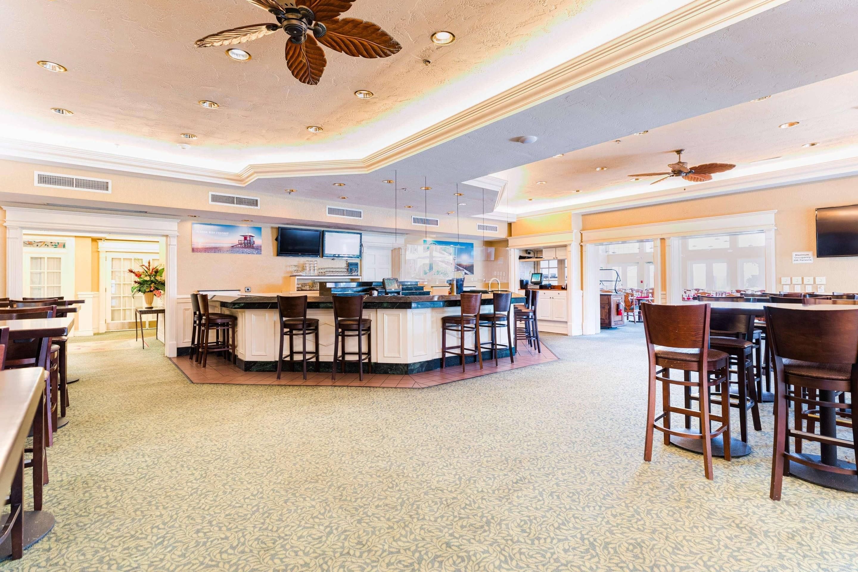 A spacious hotel lobby with a central bar area, multiple seating arrangements, and ceiling fans.