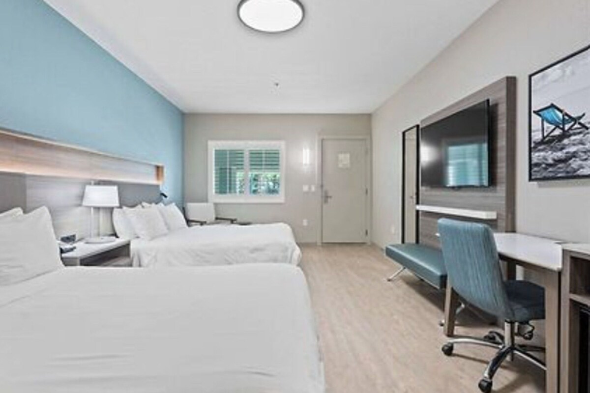 A hotel room with two beds, a desk, a chair, a television, and a window with blinds.