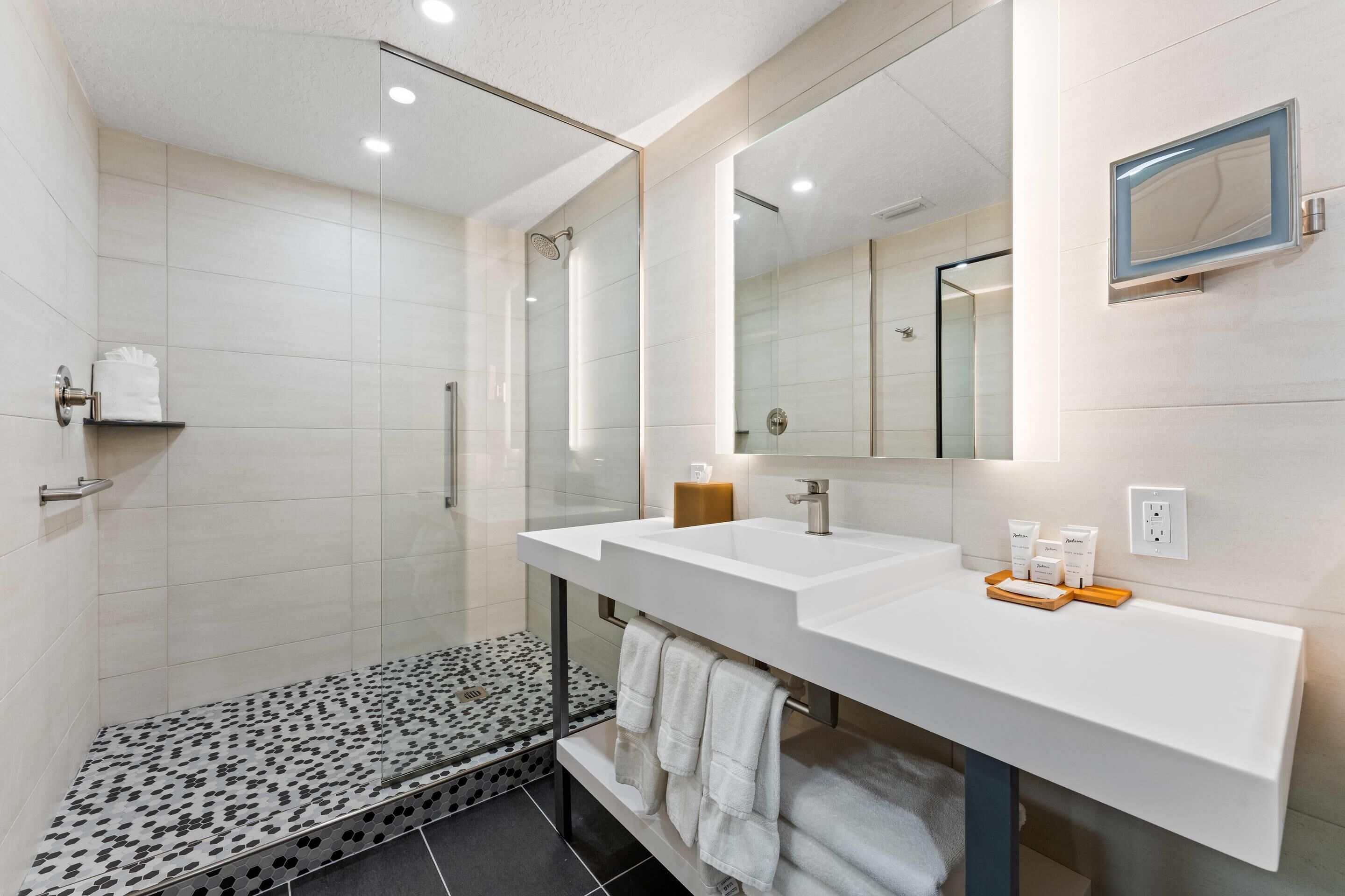 Un baño moderno con dos lavamanos, ducha y tocador con artículos de aseo.