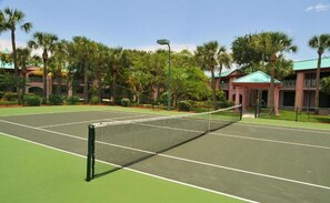A tennis court with a net, surrounded by palm trees and a building with a green roof. - Radisson Resort at the Port (Cape Canaveral)