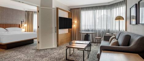 A hotel room with a bed, a sofa, a TV, a small table, and a chair.
