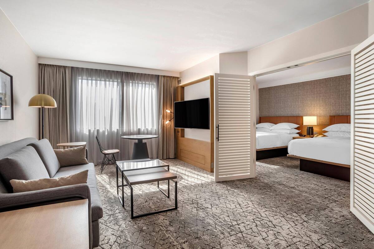 Een hotelkamer met een bank, een tafeltje, een televisie, een bed en een raam met gordijnen.