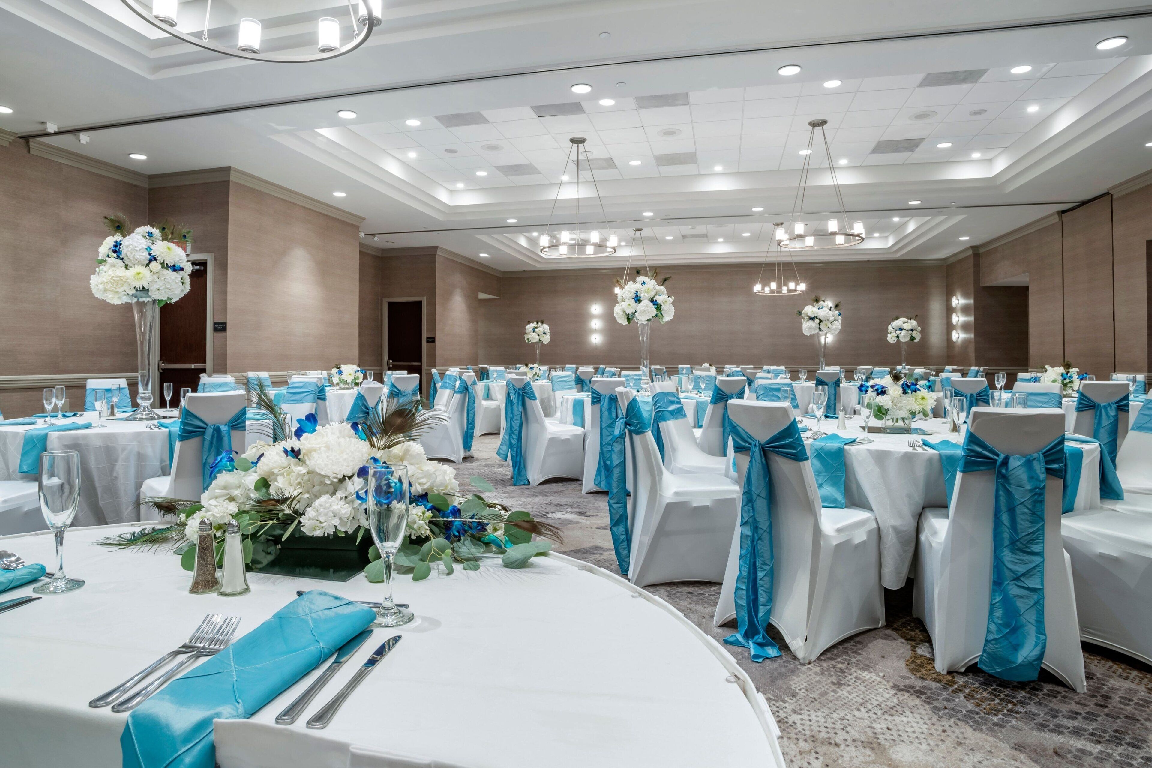 A banquet hall with round tables, white tablecloths, and chairs with blue sashes.