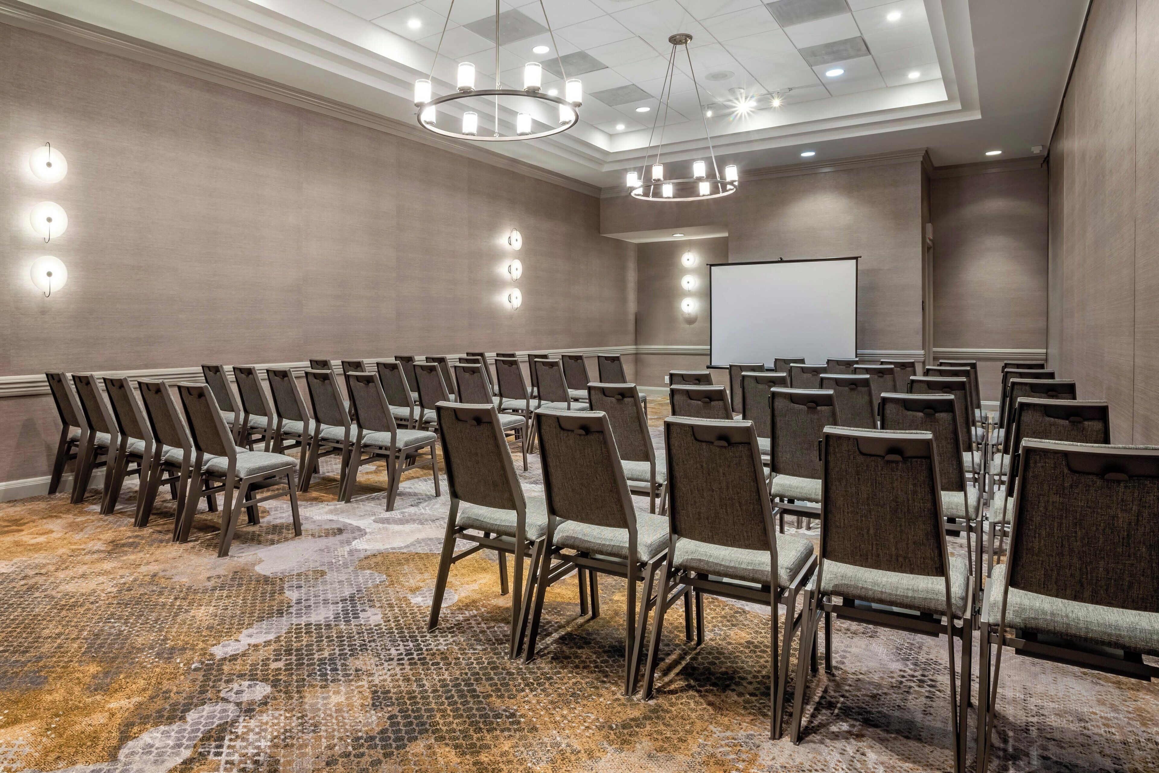 A conference room with rows of chairs, a projector screen, and a patterned carpet.