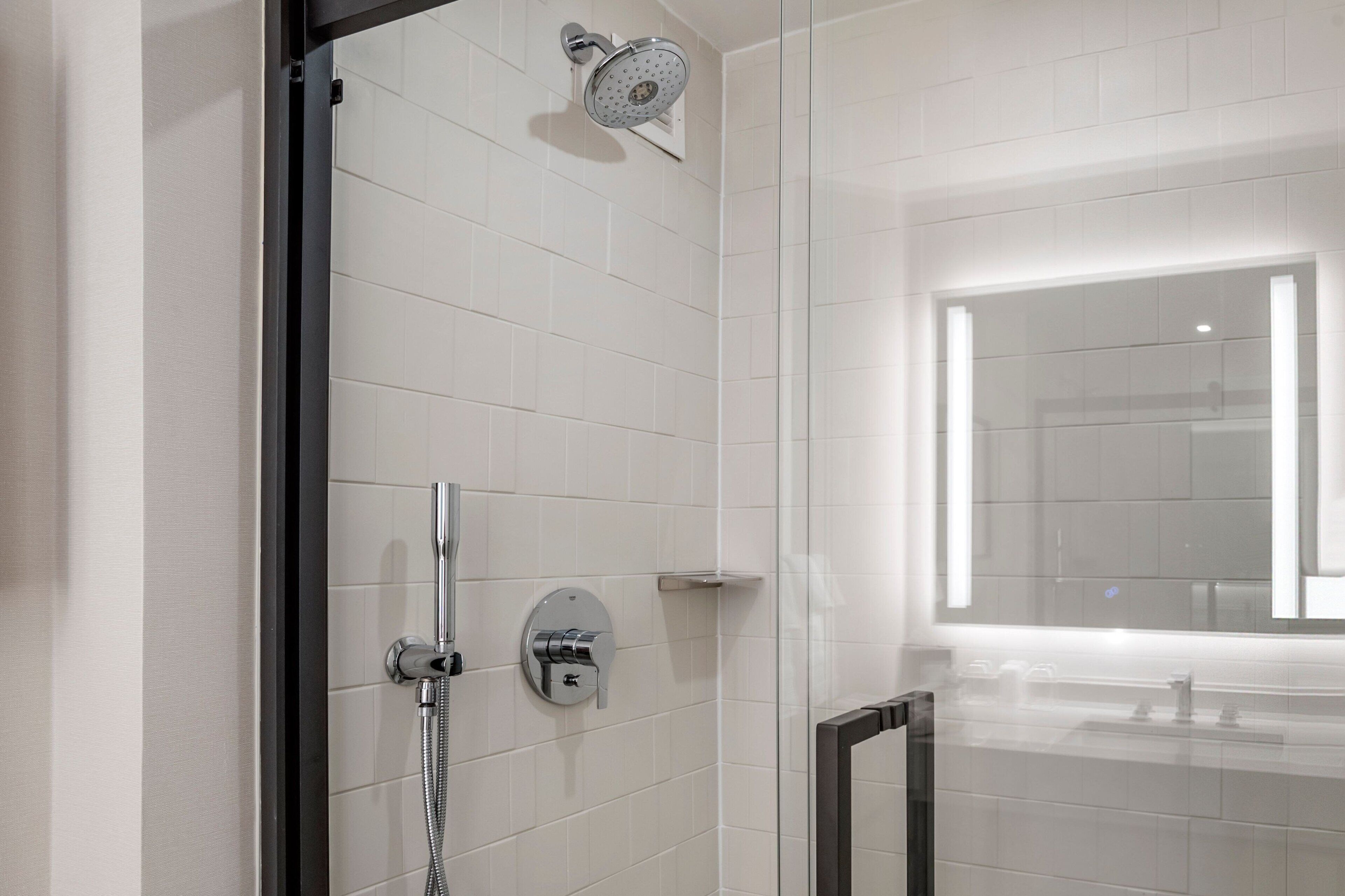 Un baño moderno con azulejos blancos, cabina de ducha de vidrio, inodoro a la vista y un espejo grande sobre el lavamanos.