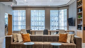 A modern lobby with a large brown sofa, two round tables, and a TV mounted on the wall.