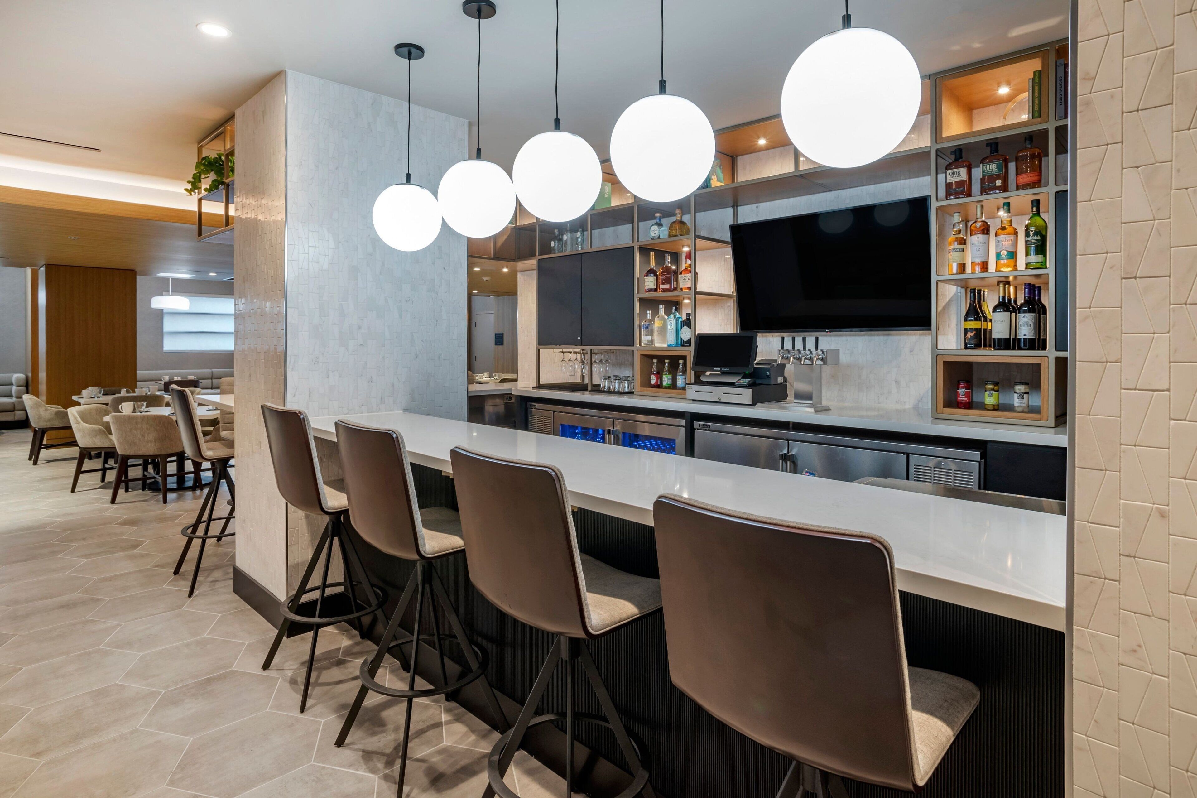 A modern bar area with a long counter, bar stools, and a variety of liquor bottles.
