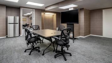 A conference room with a long table, black chairs, a flat-screen TV, and a refrigerator.