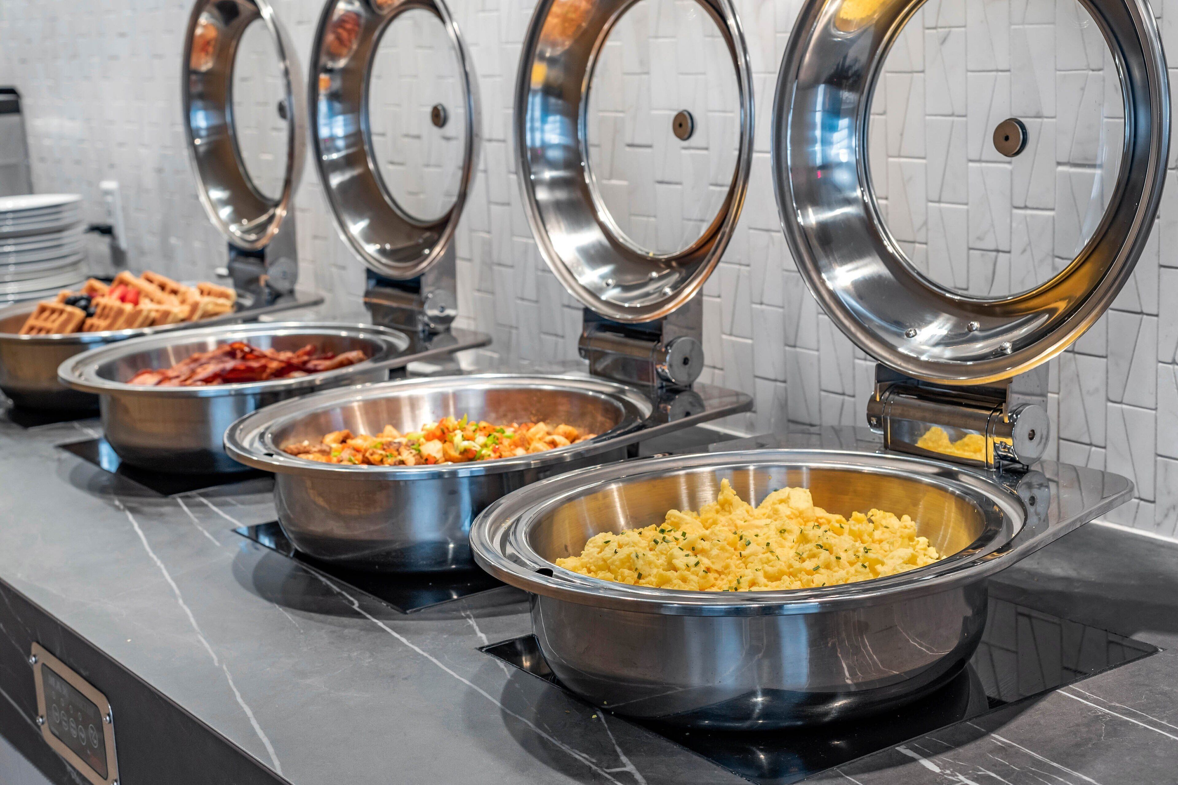 Un bufé con diversas opciones de comida, incluyendo gofres, tocino y huevos revueltos.