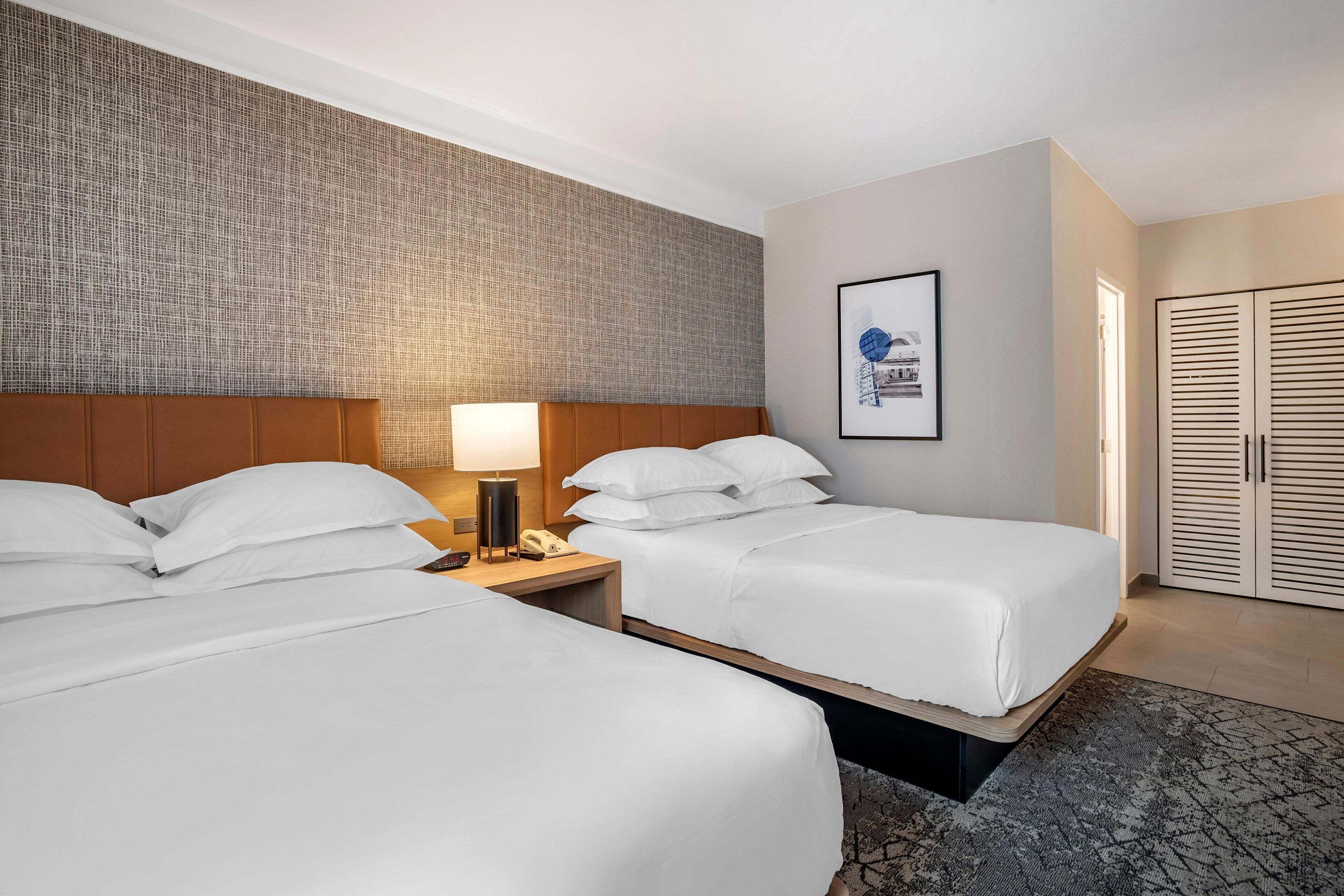 A hotel room with two beds, a nightstand with a lamp, a framed picture on the wall, and a wardrobe.