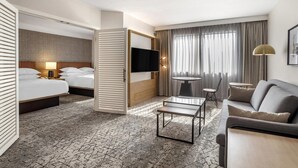 A modern hotel room with a bed, a TV, a sofa, a coffee table, and a small table with a chair.