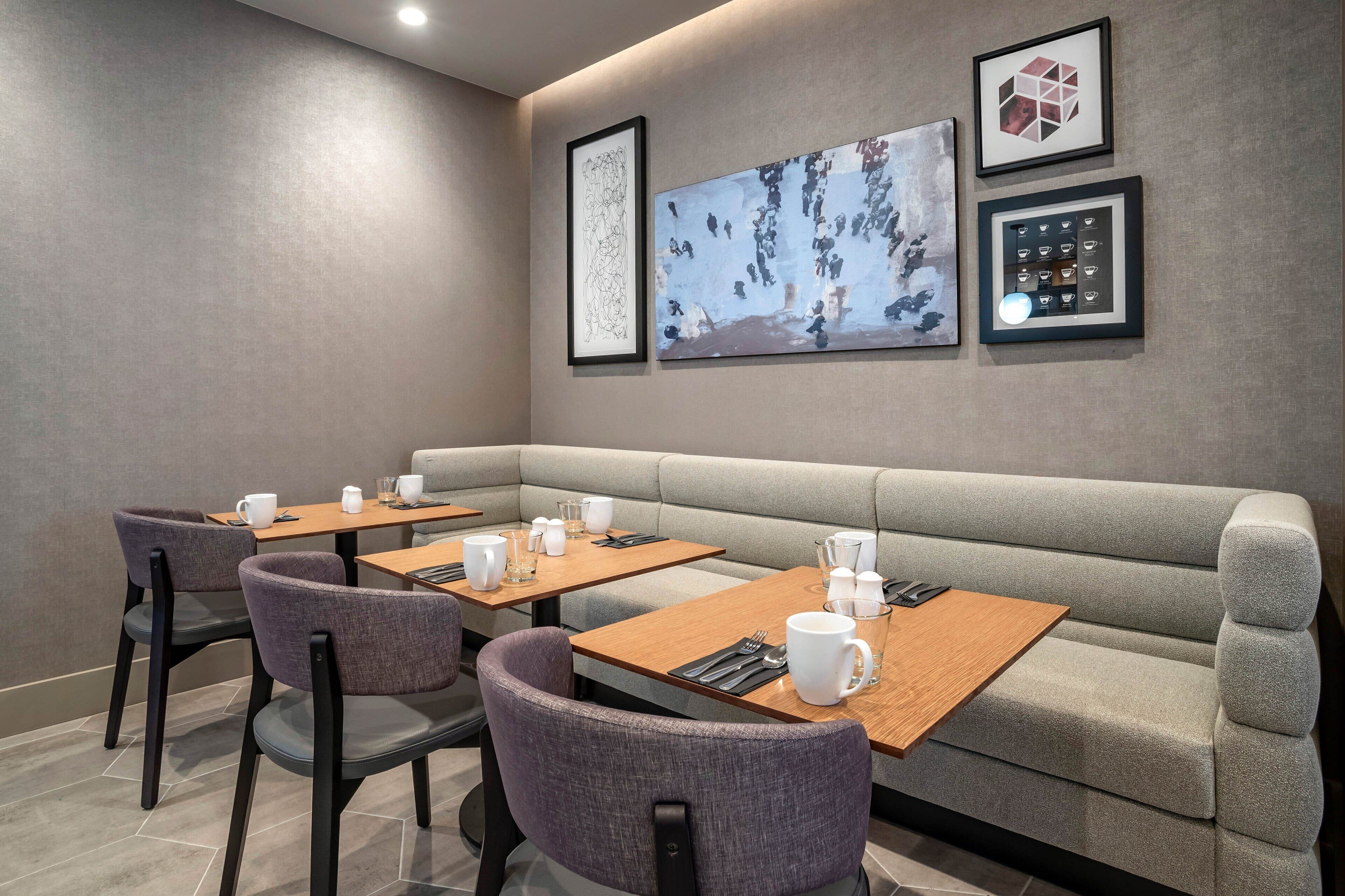 A modern dining area with a grey sofa, wooden tables, and purple chairs.