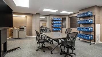 A conference room with a large table, four chairs, a TV, a printer, and shelves with boxes.