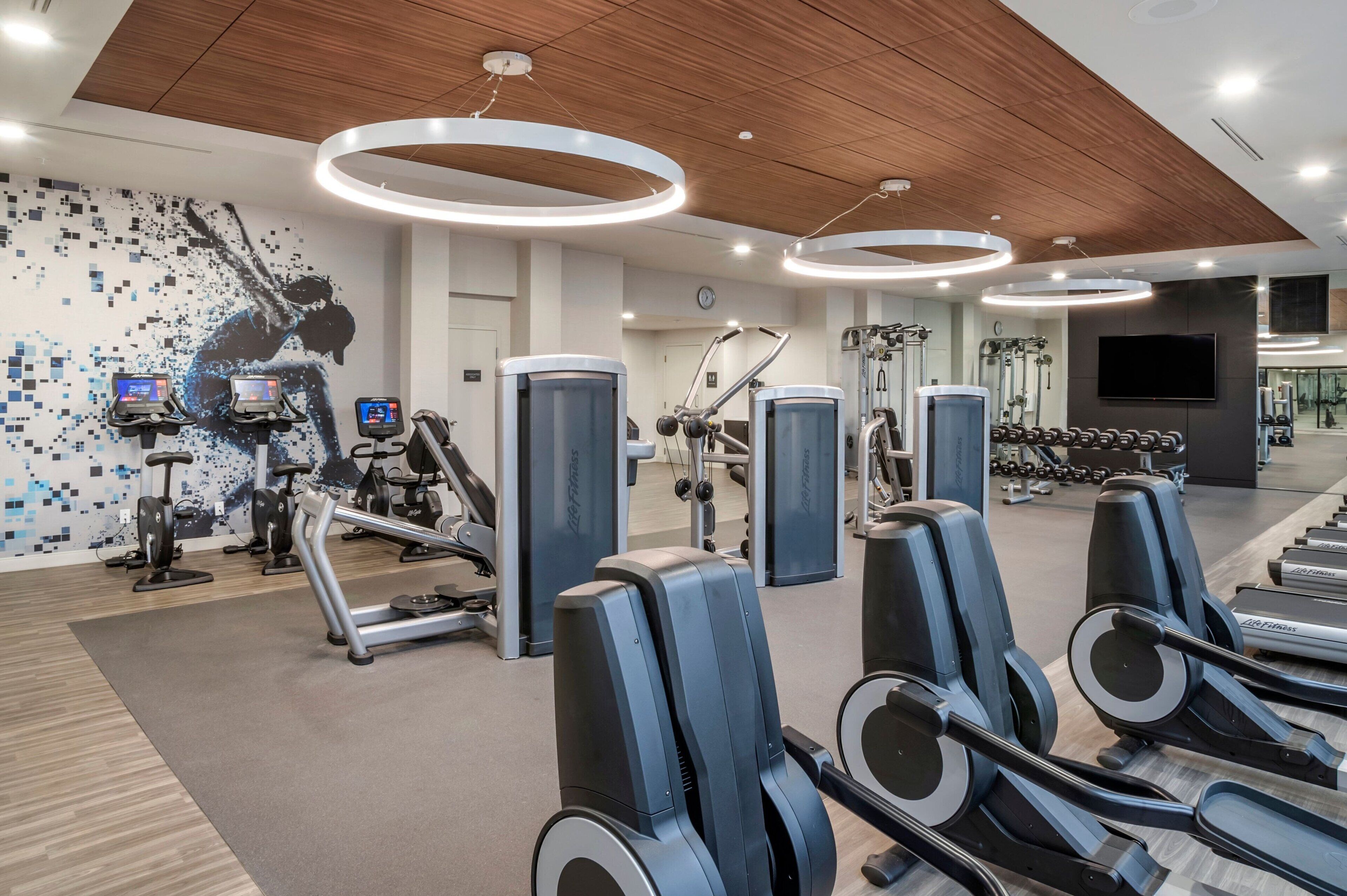 A modern gym with cardio machines, weightlifting equipment, and a digital display wall.