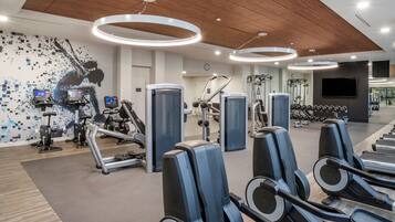 A modern gym with cardio machines, weightlifting equipment, and a digital display wall.