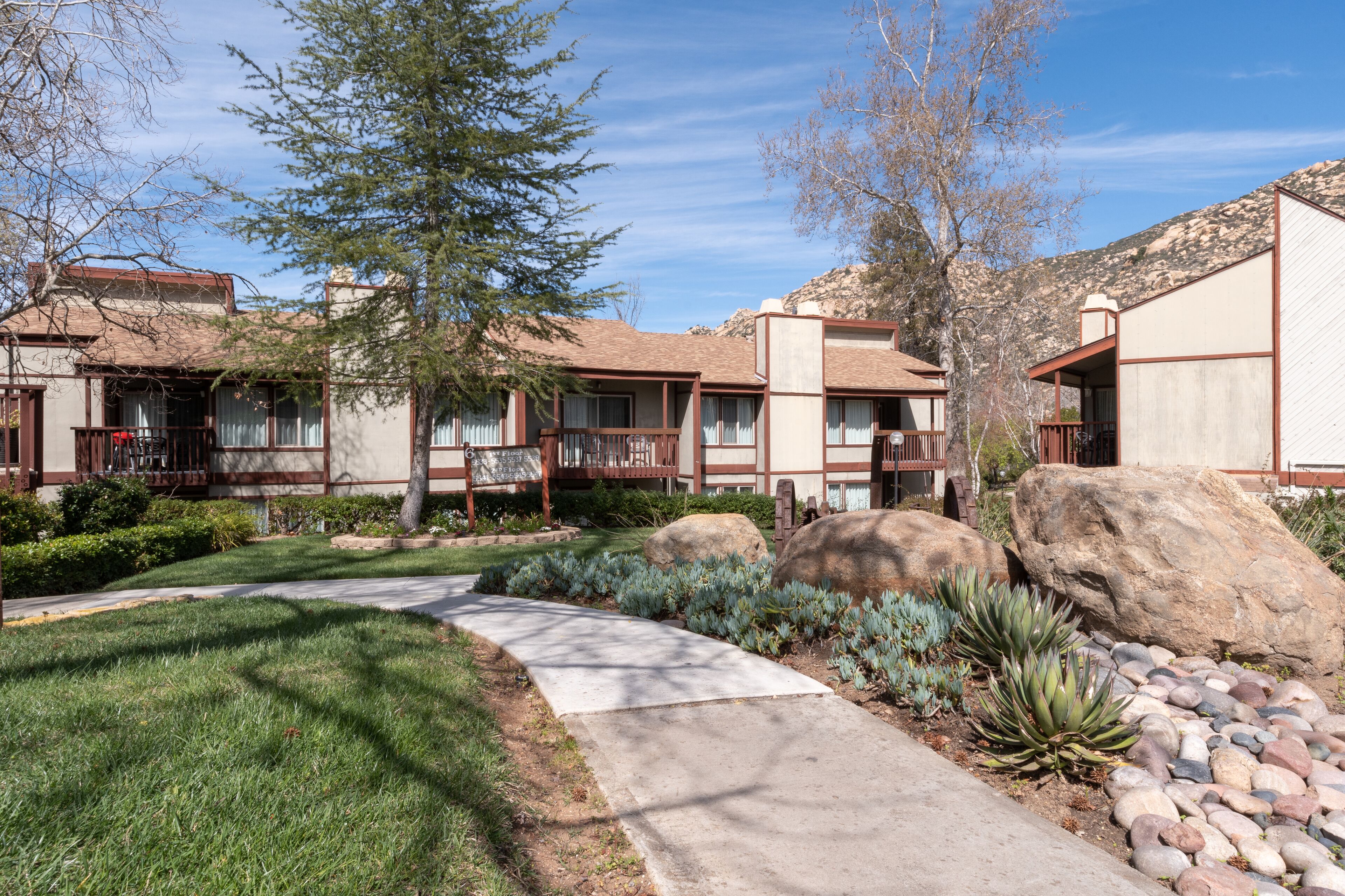 A courtyard with a pathway, large rocks, and a building with a brown roof and white walls.