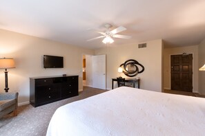 A hotel room with a bed, a television, a desk, a chair, a ceiling fan, and a door.