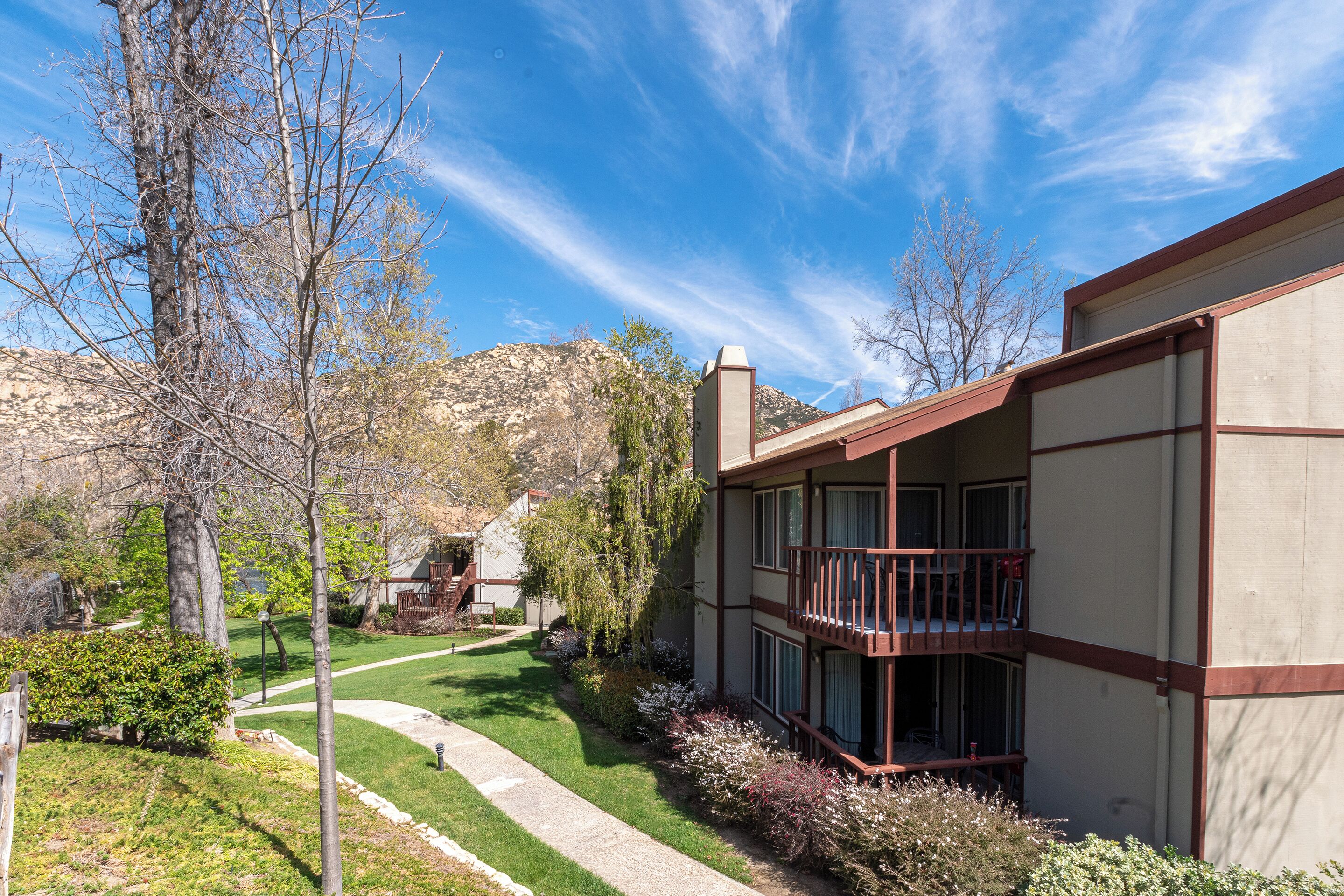 A two-story building with a balcony, a well-maintained lawn, and a mountain backdrop.