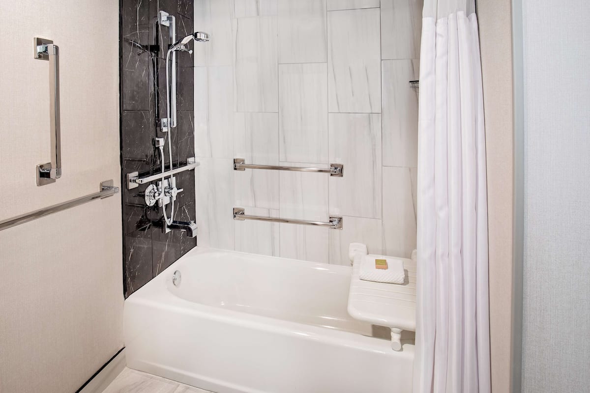 Une salle de bain moderne avec une baignoire blanche, une douche dotée d’une porte en verre et une barre d’appui.